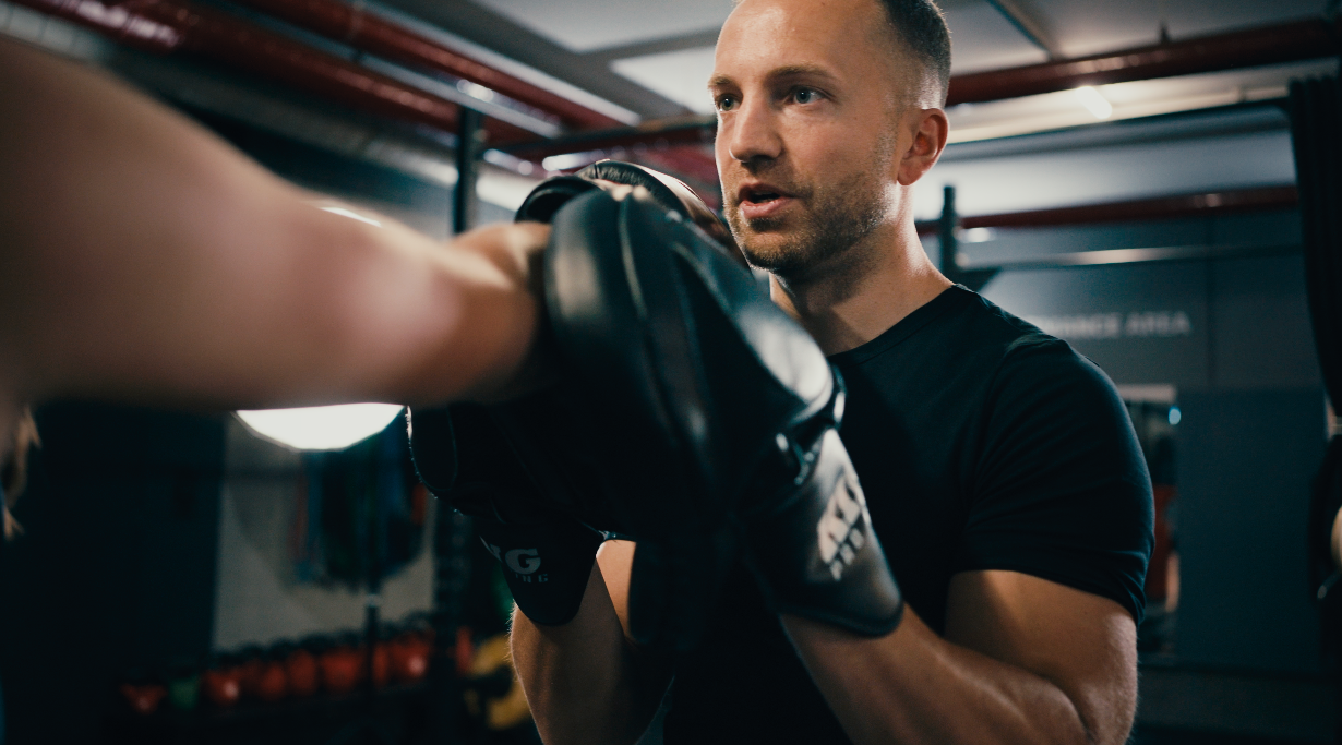 Trainer hält die Pratzen, ein Teilnehmer schlägt beim Boxtraining hinein